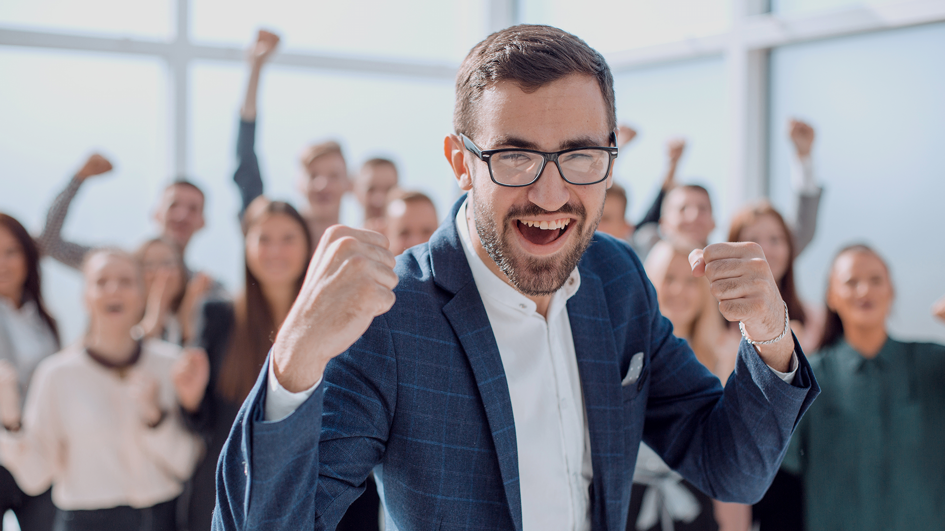 Líder de negócios comemorando sucesso com equipe motivada ao fundo, todos demonstrando energia e conquista em ambiente corporativo moderno